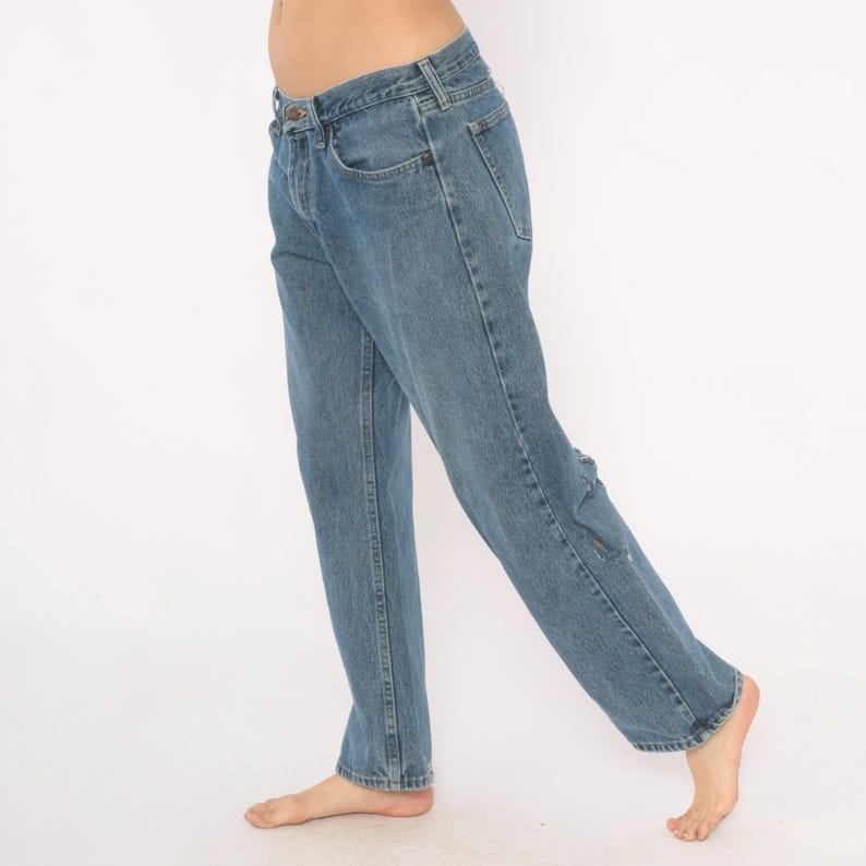 May include: Light blue denim jeans with a classic five-pocket design. The jeans have a straight leg cut and a faded wash, with a small distressed area on the right leg. The jeans are shown against a white background.