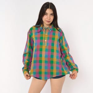 May include: A long-sleeved button-down shirt featuring a vibrant plaid pattern in shades of mustard yellow, bright green, magenta, and teal. The shirt has a classic collar, a partial button placket down the center front, and long sleeves with cuffs.