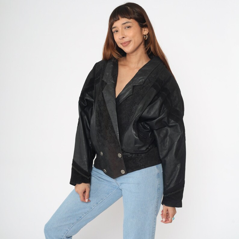 May include: A black leather jacket with a double-breasted closure and a textured pattern. The jacket has a collar and long sleeves.