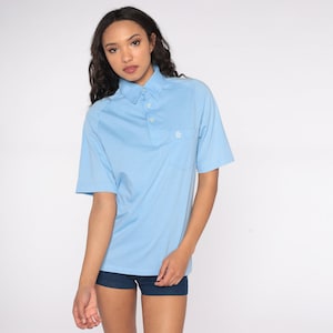 May include: A light blue short-sleeved polo shirt with a white button-down collar and a small embroidered logo on the left chest.