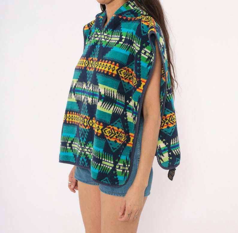 May include: A sleeveless hooded poncho featuring a vibrant geometric pattern in shades of navy blue, teal, bright green, yellow, and orange. The garment has an open-side design with dark blue trim along the edges and a hood at the neckline.