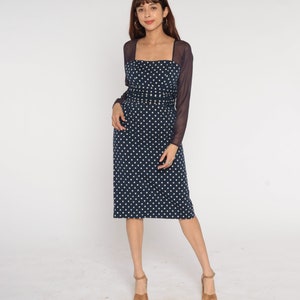 May include: A navy blue midi dress with white polka dots and a sheer black long-sleeved overlay. The dress has a square neckline and a fitted silhouette.