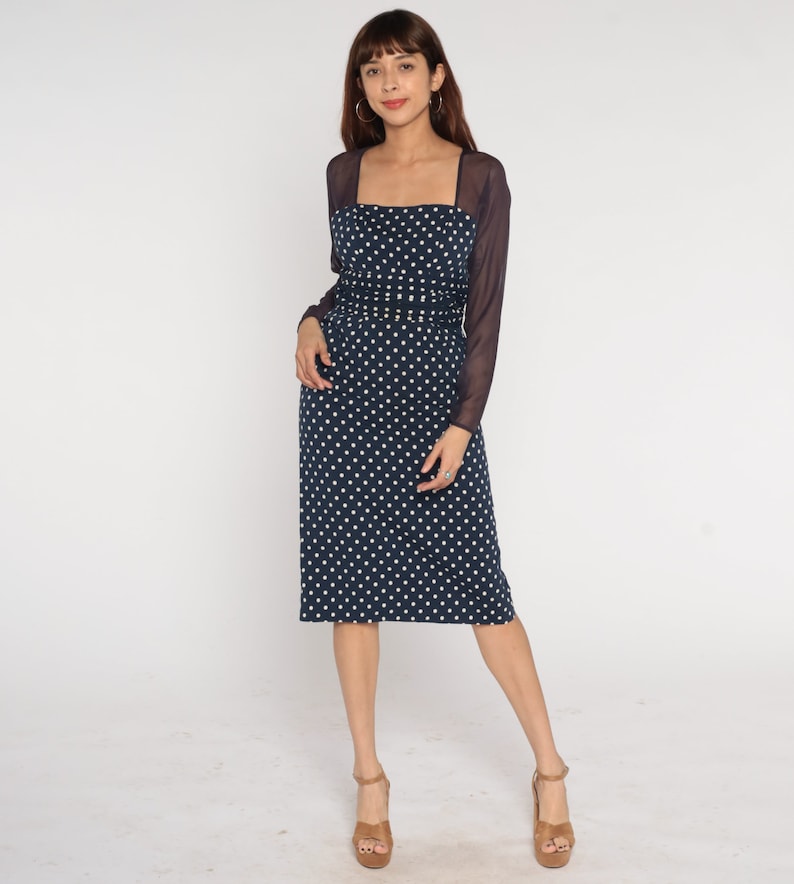 May include: A navy blue midi dress with white polka dots and a sheer black long-sleeved overlay. The dress has a square neckline and a fitted silhouette.