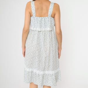 May include: A white midi dress with a blue floral print and lace trim. The dress has a square neckline and thin straps.