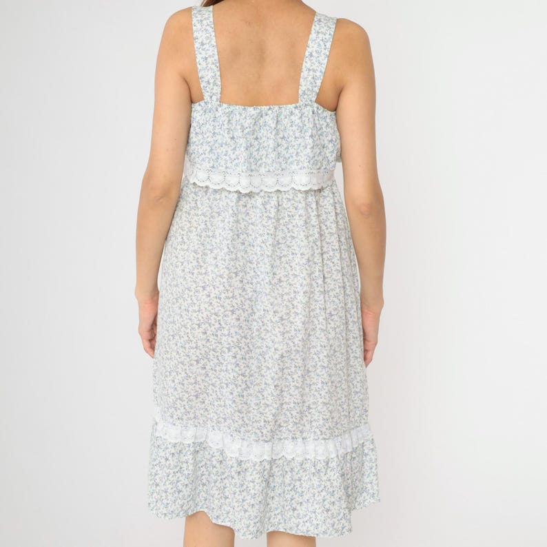 May include: A white midi dress with a blue floral print and lace trim. The dress has a square neckline and thin straps.