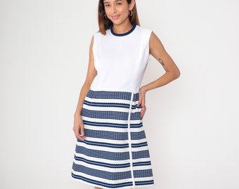 Puede incluir: Un vestido blanco sin mangas con una falda de rayas azules y blancas. El vestido tiene un ribete azul marino alrededor del escote.