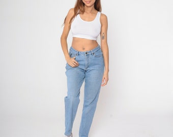 May include: A white tank top and light blue jeans. The jeans have a classic, straight-leg fit. The model is wearing white sneakers. The background is plain white.