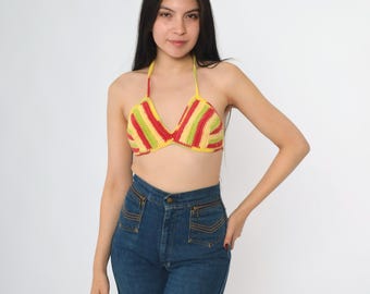 May include: A colorful crochet halter top with red, yellow, and green stripes. The top is paired with high-waisted blue denim jeans. The halter top is a vibrant piece of handmade clothing.