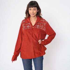 Könnte beinhalten: Ein langärmliges Hemd in Rostfarbe mit Kragen und Stickereien an den Schultern. Die Stickerei ist in Weiß-, Silber- und Goldtönen gehalten.