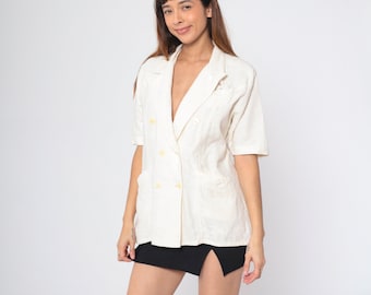 May include: A white linen blazer with a double-breasted closure and short sleeves. The blazer has a textured pattern and yellow buttons.