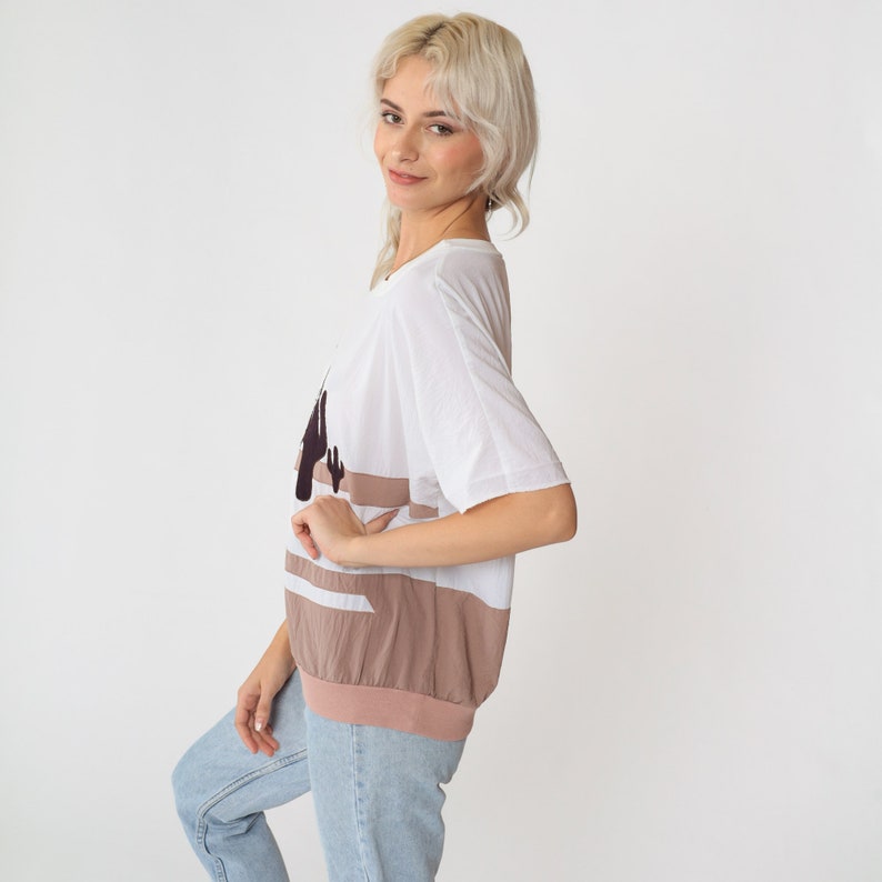 May include: An oversized white and brown striped t-shirt with a black cactus graphic. The shirt has a relaxed fit and short sleeves.