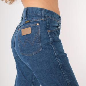 May include: A pair of blue denim jeans with a brown leather patch on the back pocket that says "Wrangler".