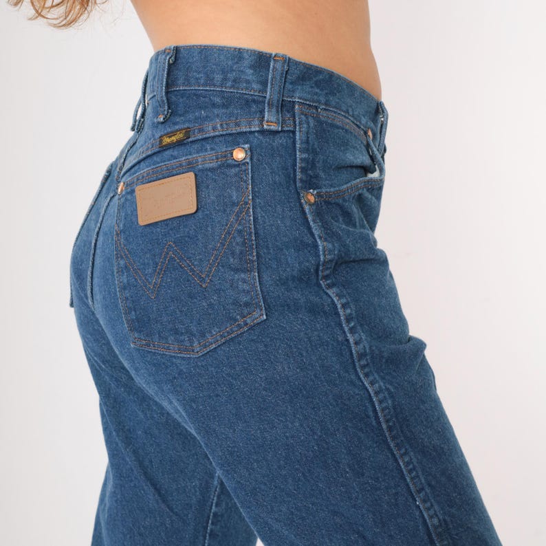 May include: A pair of blue denim jeans with a brown leather patch on the back pocket that says "Wrangler".