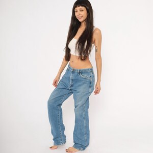 Pu&ograve; includere: Jeans di denim blu chiaro con vestibilit&agrave; rilassata. I jeans hanno un classico design a cinque tasche e gamba dritta. La modella indossa una canotta bianca. Lo sfondo &egrave; bianco.