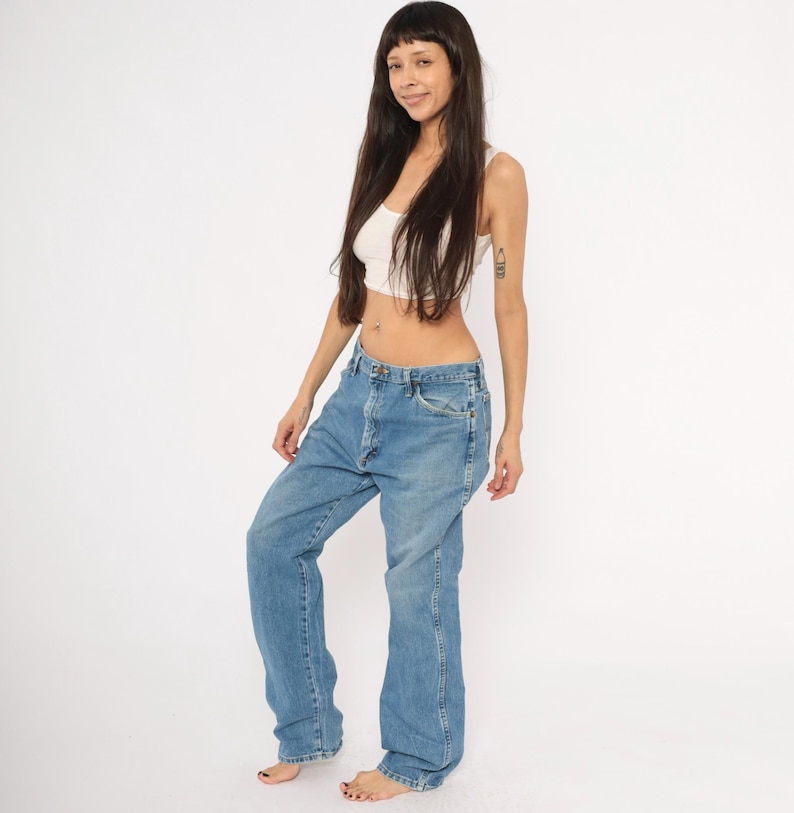 Pu&ograve; includere: Jeans di denim blu chiaro con vestibilit&agrave; rilassata. I jeans hanno un classico design a cinque tasche e gamba dritta. La modella indossa una canotta bianca. Lo sfondo &egrave; bianco.