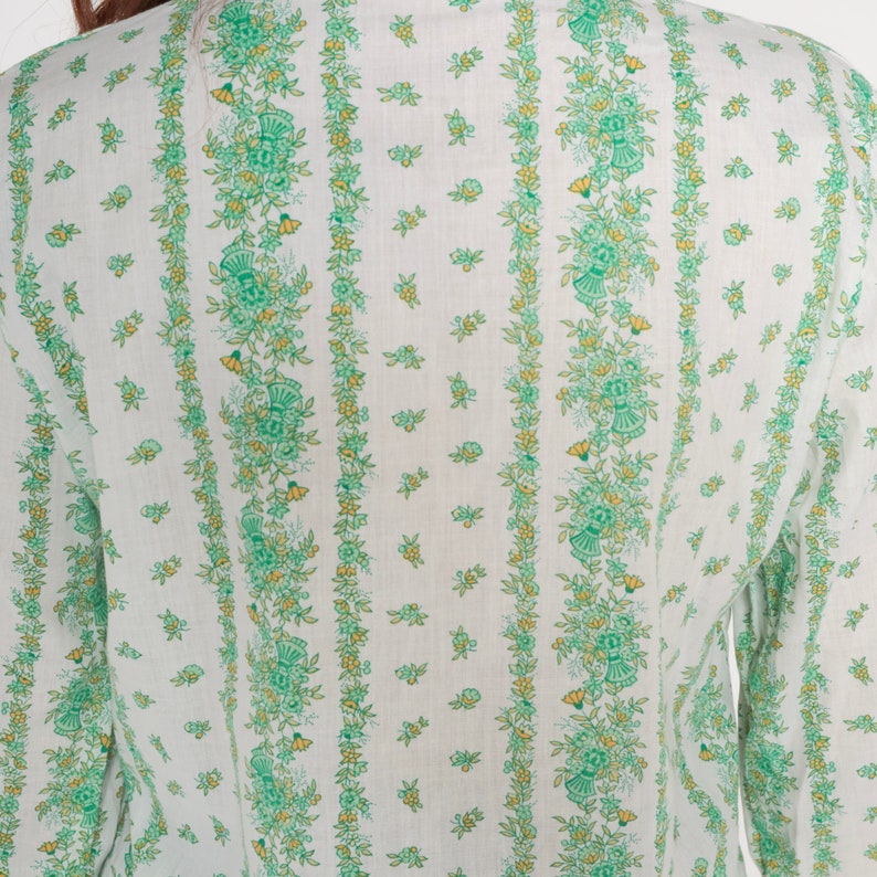 Puede incluir: Camisa blanca de manga larga con estampado floral verde y amarillo.