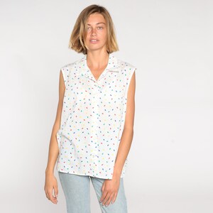 May include: White sleeveless collared shirt with a colorful leaf pattern. The shirt has a button-down front and a relaxed fit. The leaves are in red, yellow, blue, and green.