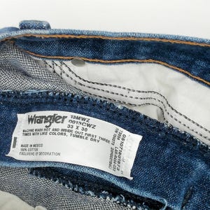 May include: Close-up of the inside of blue denim Wrangler jeans. The label reads "Wrangler 13MWZ 33 X 30". The jeans have a classic five-pocket design and are made of 100% cotton. The inseam is 30 inches.