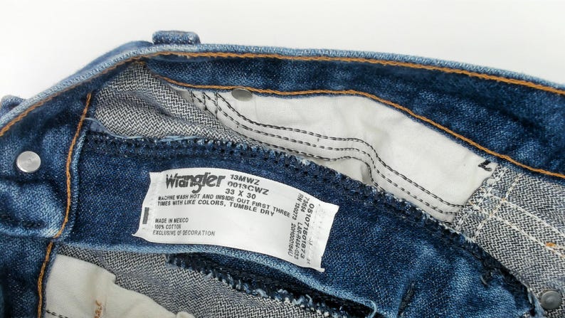 May include: Close-up of the inside of blue denim Wrangler jeans. The label reads "Wrangler 13MWZ 33 X 30". The jeans have a classic five-pocket design and are made of 100% cotton. The inseam is 30 inches.