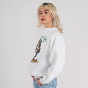 May include: White sweatshirt with a green and white graphic of a woman holding a beer mug. The graphic includes the text "O'Brien's" and "Est. 1814".