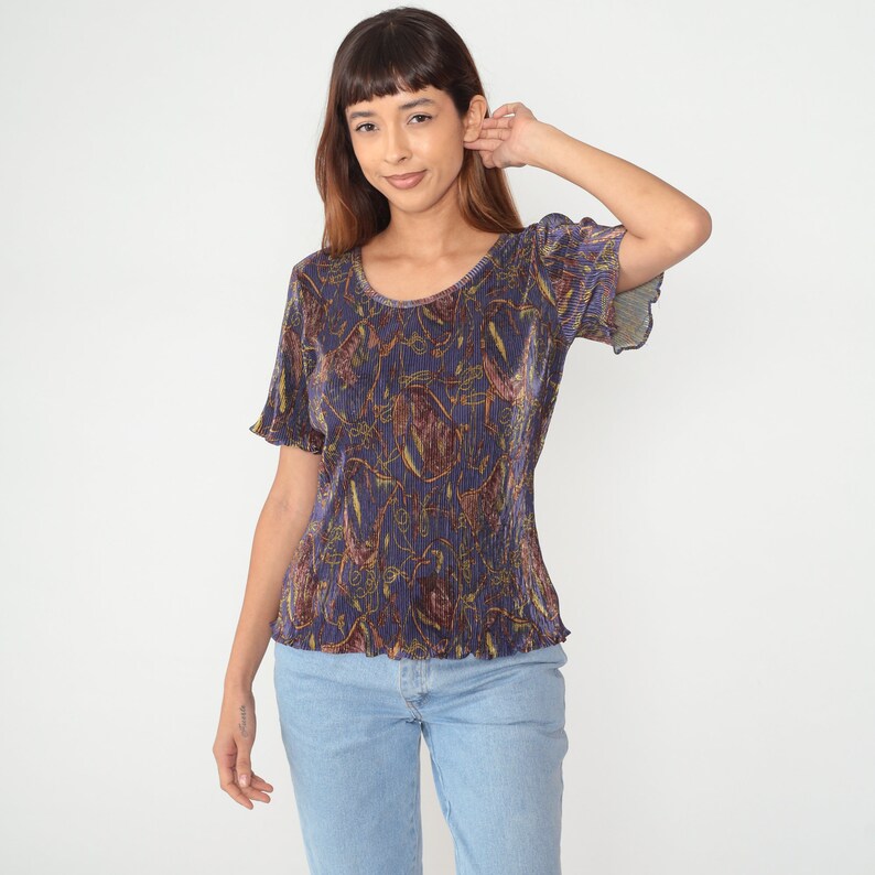 Puede incluir: Una camisa de manga corta azul y dorada con estampado y cuello redondo.