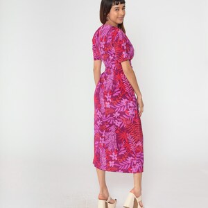 May include: A pink midi dress with a floral print featuring red, pink, and white flowers and leaves. The dress has a V-neckline and short sleeves.