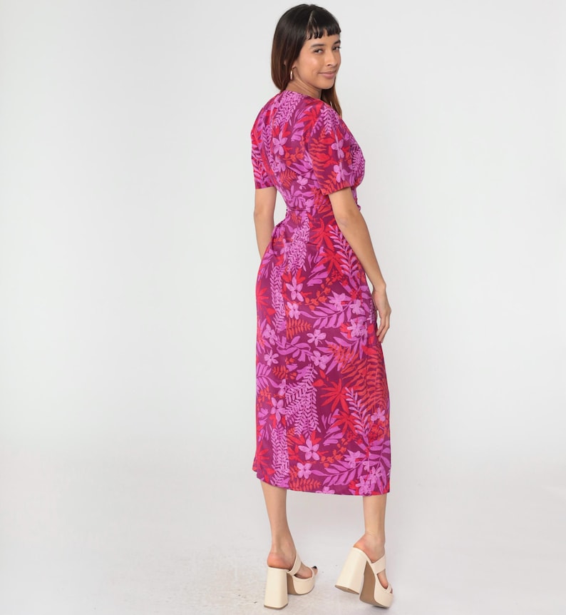 May include: A pink midi dress with a floral print featuring red, pink, and white flowers and leaves. The dress has a V-neckline and short sleeves.