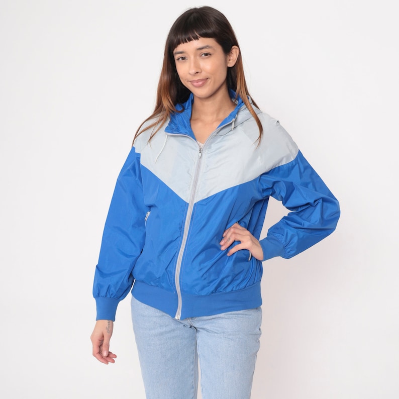 May include: A blue and gray hooded jacket with a zipper closure. The jacket has a color block design with a chevron pattern.