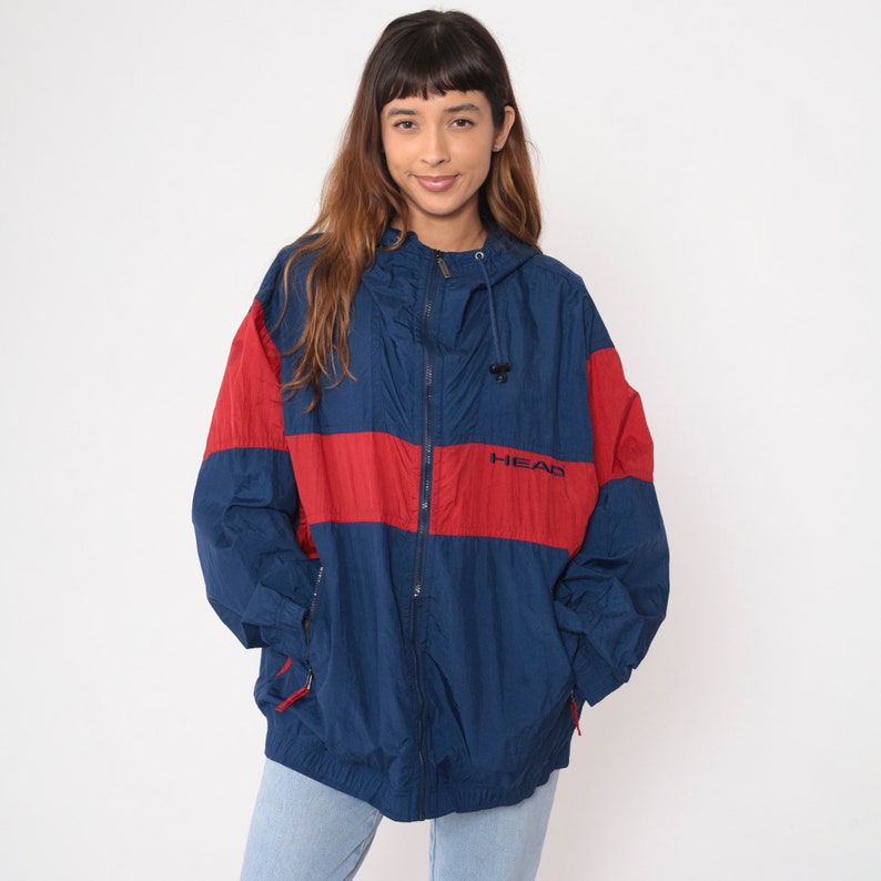May include: A blue and red windbreaker jacket with a zipper closure and a hood. The jacket has the word "HEAD" printed on the front in black.