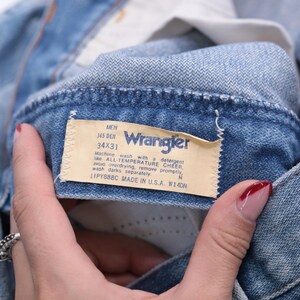 May include: Close-up of a light blue denim Wrangler jeans label. The label reads "MEN 345 DEN 34X31" and includes washing instructions. Made in the U.S.A.