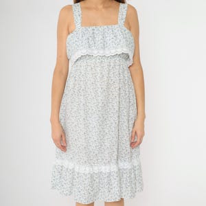 May include: A white midi dress with a blue floral print and white lace trim. The dress has a square neckline and thin straps.