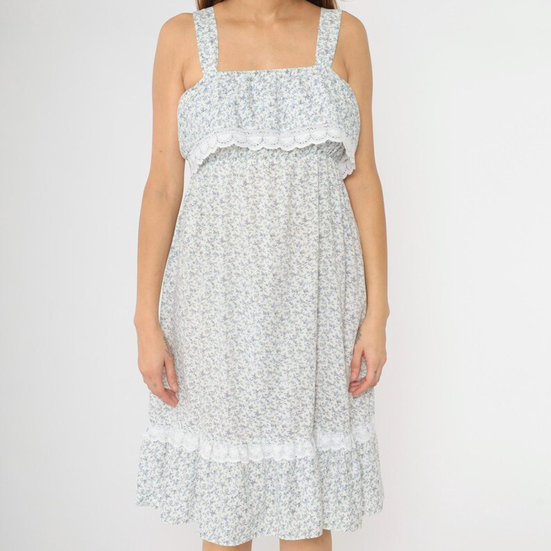 May include: A white midi dress with a blue floral print and white lace trim. The dress has a square neckline and thin straps.