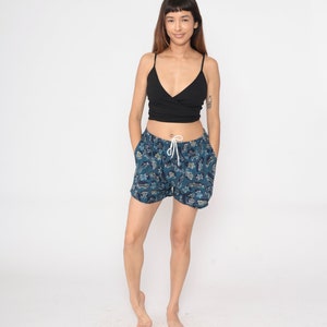May include: A woman wearing a black tank top and blue and white patterned shorts. The shorts have a drawstring waist and are made of a lightweight fabric.