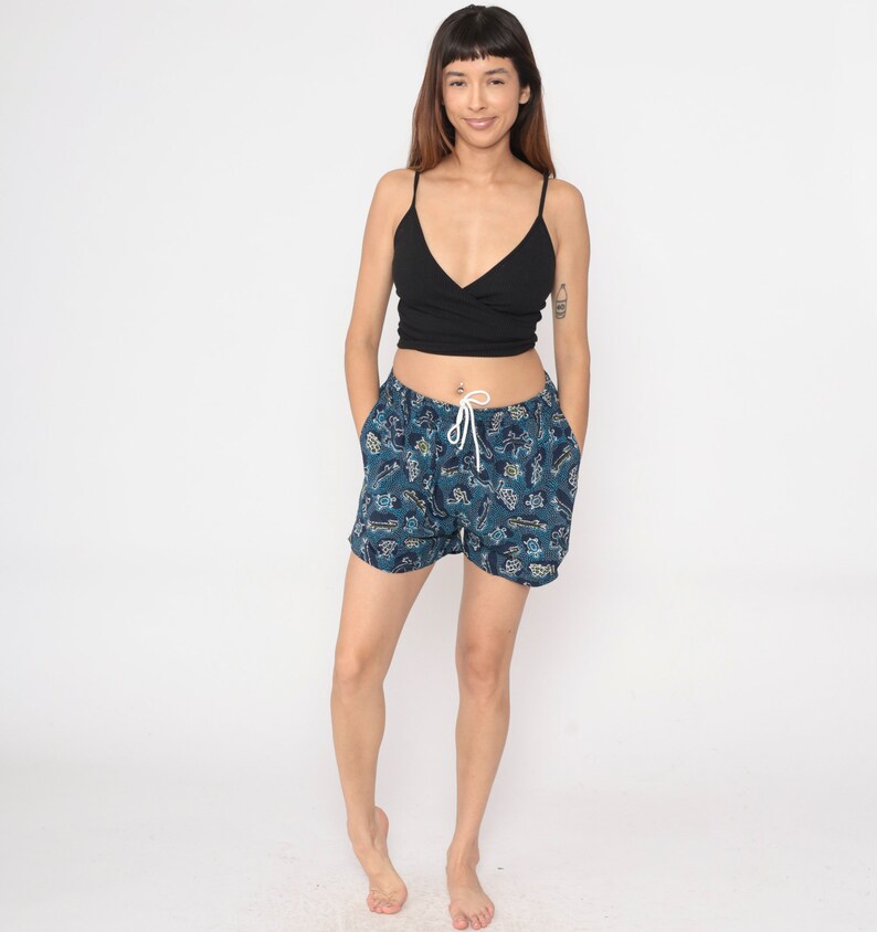 May include: A woman wearing a black tank top and blue and white patterned shorts. The shorts have a drawstring waist and are made of a lightweight fabric.