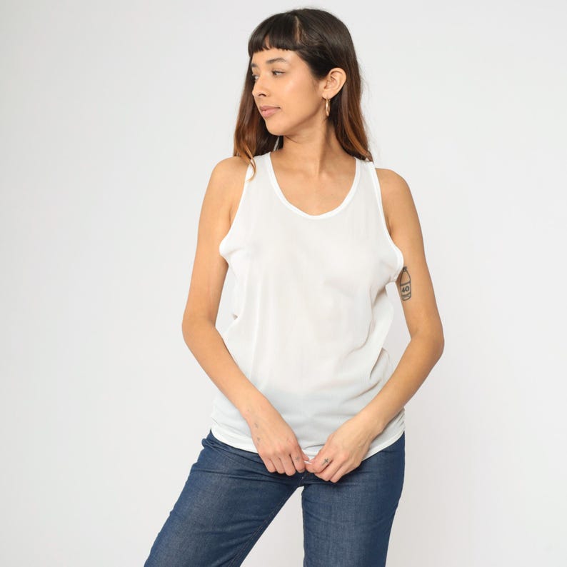 Peut inclure: Un d&eacute;bardeur blanc &agrave; col rond. Le haut sans manches est fait d'une mati&egrave;re l&eacute;g&egrave;re. Le mod&egrave;le porte un jean bleu. Le fond est blanc uni.