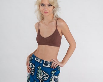 Op de afbeelding: Een bruine geribbelde gebreide bralette en een blauwe short met patroon. De short heeft een levendige blauwe achtergrond met witte en groene geometrische ontwerpen. De bralette heeft dunne bandjes en een V-hals.