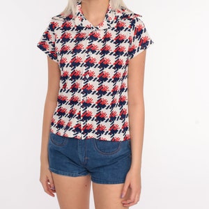 May include: A white button-up shirt with a red and blue houndstooth pattern. The shirt has short sleeves and a collar.