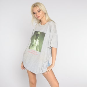 May include: A gray oversized t-shirt with a vintage image of a woman in a nurse's uniform. The text on the shirt reads "Celebrate Nursing! past..."