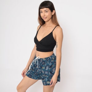 May include: A woman wearing a black crop top and blue and white patterned shorts. The shorts have a drawstring waist and feature a variety of small designs, including animals and geometric shapes.