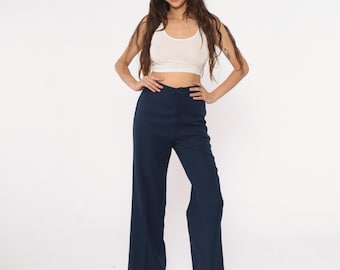Puede incluir: Pantalones anchos azul marino. Los pantalones tienen cintura alta y diseño acampanado. La modelo lleva un top blanco y tacones de plataforma beige. El fondo es blanco liso.