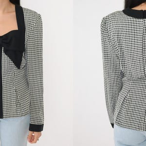 May include: A black and white gingham patterned blouse with a black bow at the neckline. The blouse has long sleeves and a fitted silhouette.