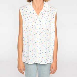 May include: White sleeveless button-down shirt with a colorful confetti pattern. The shirt features a collared neckline and a series of small, colorful teardrop shapes in red, blue, yellow, and green scattered across the fabric.