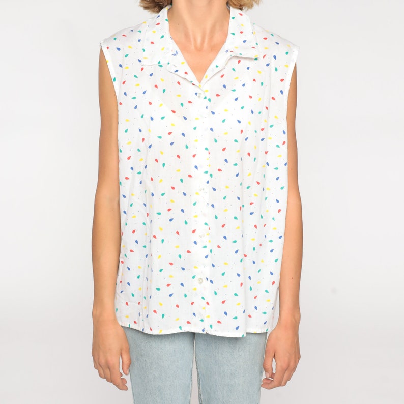 May include: White sleeveless button-down shirt with a colorful confetti pattern. The shirt features a collared neckline and a series of small, colorful teardrop shapes in red, blue, yellow, and green scattered across the fabric.