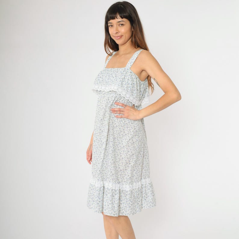 May include: A white dress with a floral print and lace trim. The dress has a square neckline and thin straps.