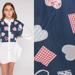 May include: White button-down shirt with a blue panel featuring a patchwork design of hearts, squares, and stripes in red, white, and blue.