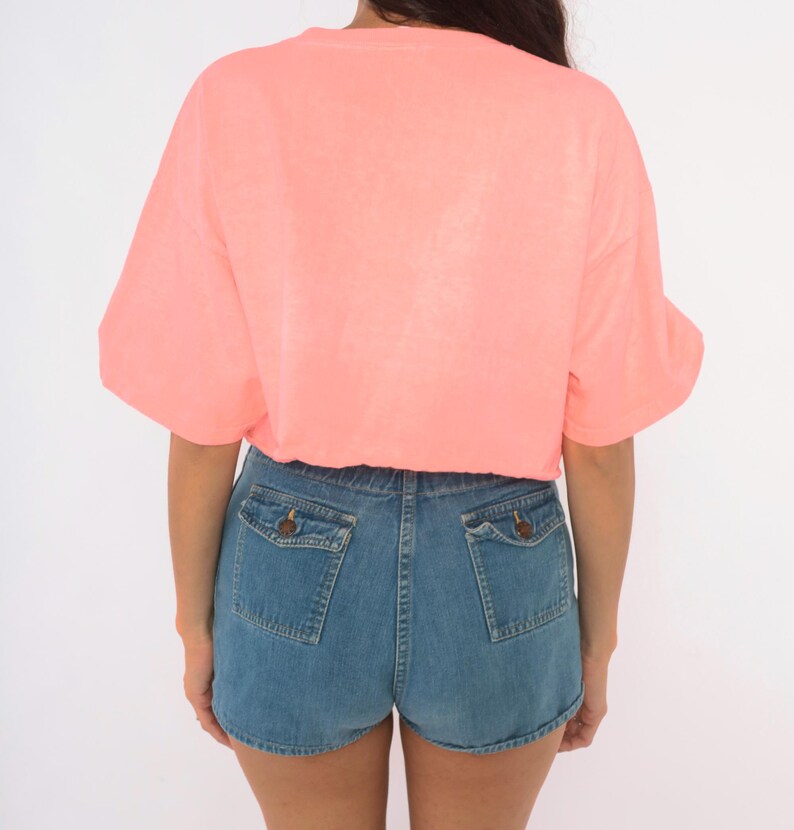 K&ouml;nnte beinhalten: Ein leuchtend neon-korallenfarbenes T-Shirt mit kurzen &Auml;rmeln, kombiniert mit mittelblauen Jeansshorts. Die Shorts verf&uuml;gen &uuml;ber zwei Ges&auml;&szlig;taschen mit gekn&ouml;pften Klappen und einen klassischen Saum, was einen l&auml;ssigen Look mit einem Oberteil ergibt.