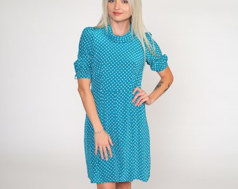 May include: A turquoise blue dress with white polka dots. The dress has a mock neck and short sleeves.