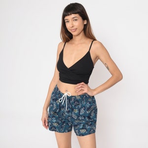 May include: Blue and green patterned shorts with a white drawstring. The shorts have a variety of small designs, including circles, dots, and lines.