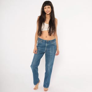 Peut inclure: Jean bleu en denim avec des coutures blanches sur le devant et les c&ocirc;t&eacute;s. Le jean a une conception classique &agrave; cinq poches et une coupe droite. Le jean est de couleur moyenne et semble vintage.