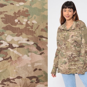 Pode incluir: Uma camisa de manga comprida com padrão de camuflagem, fechamento frontal com botões e um bolso de remendo na manga esquerda.